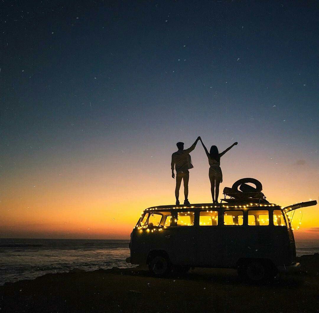 Two travellers celebrating on the roof of a camper van at sunset